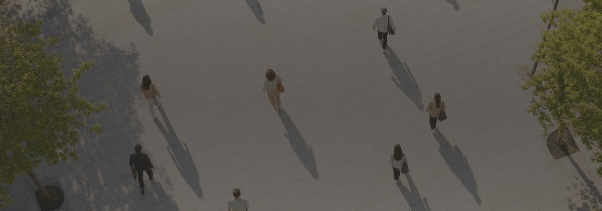 Seen from above: a dozen people crossing a sunlit city square in the morning, each walking a different way, each one alone